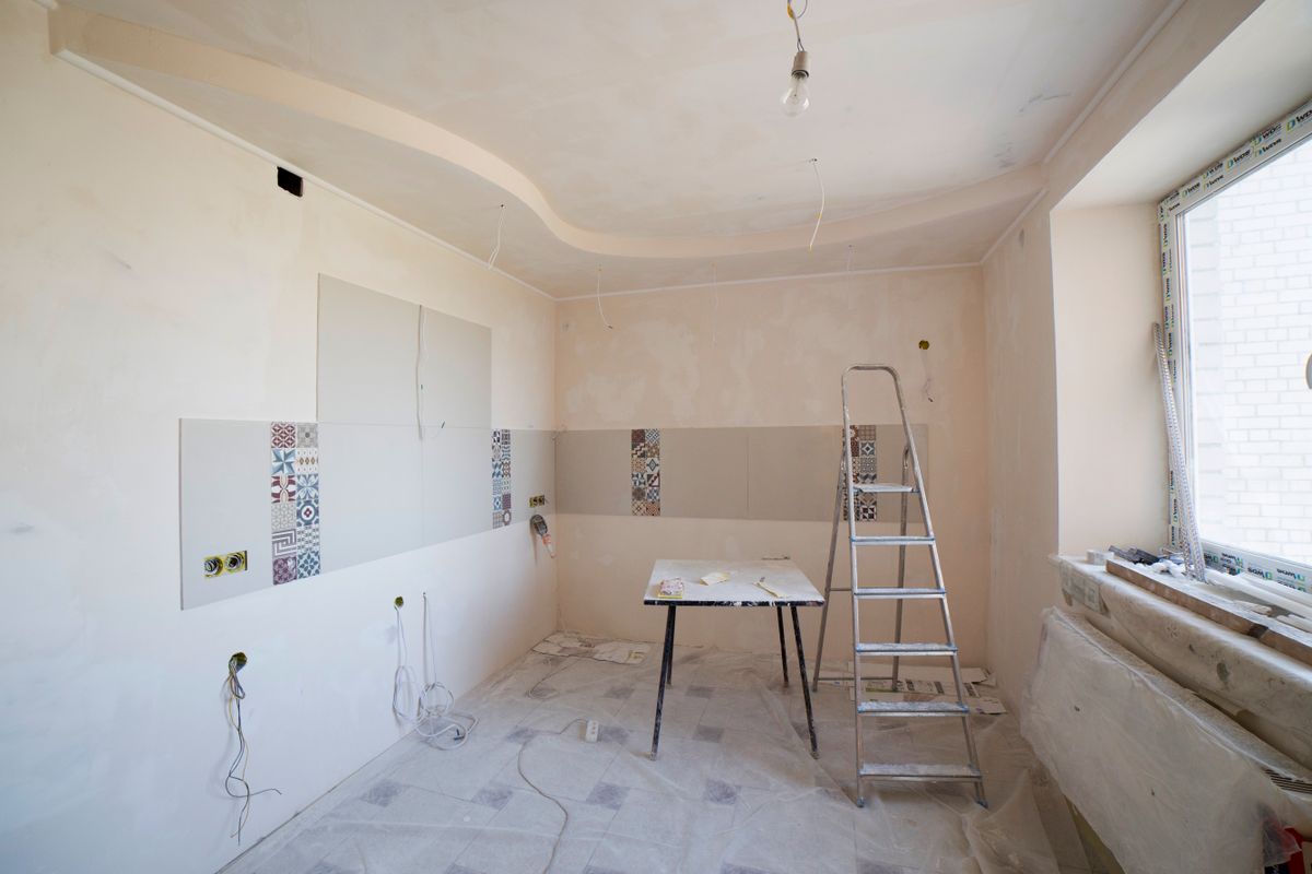 Kitchen mid-renovation with a stepladder, drop cloths on the floor, and freshly finished ceiling and walls